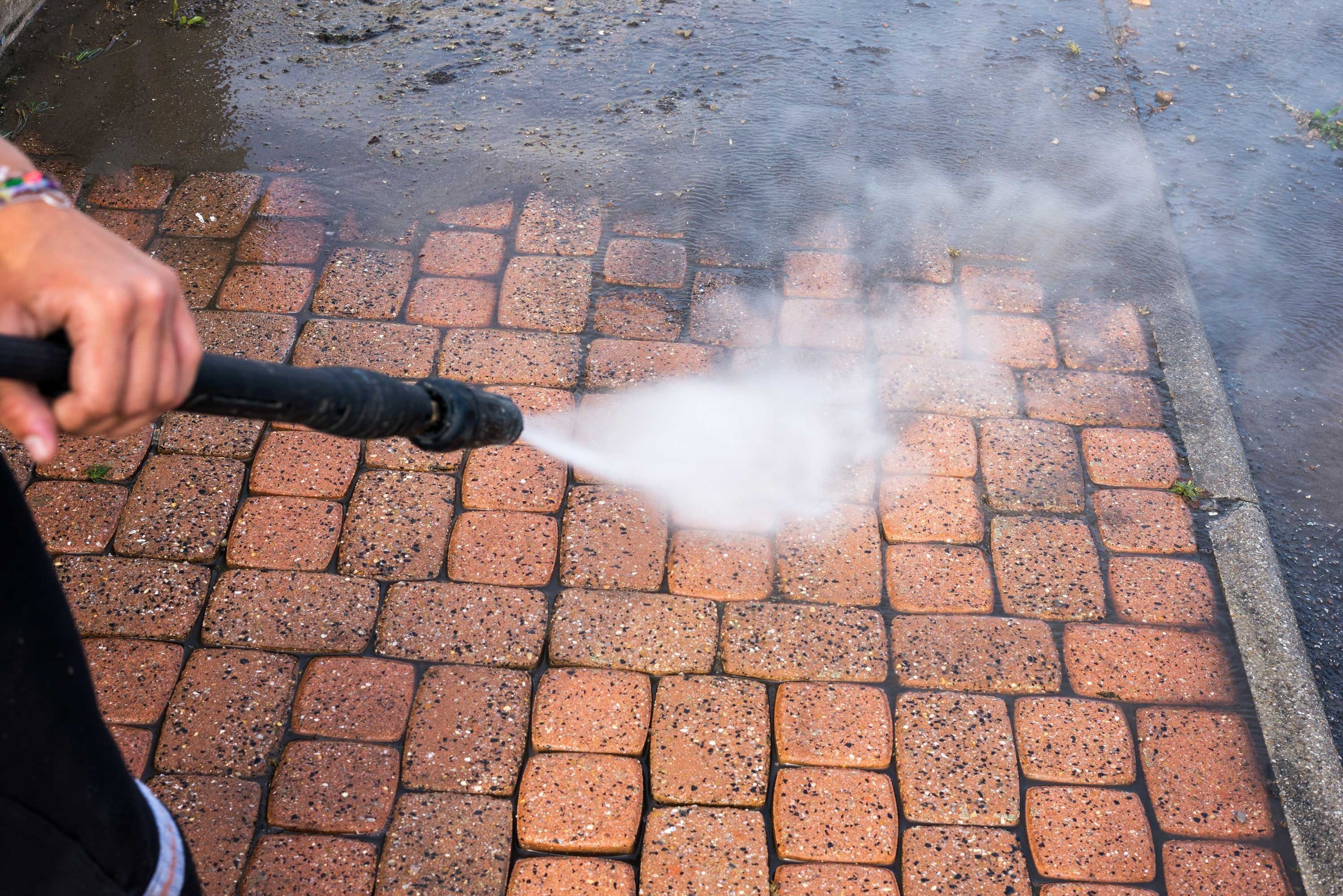 person powerwashing bricks on a pavement